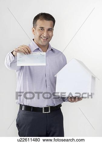 Stock Image - Man holding a house model and cheque. Fotosearch