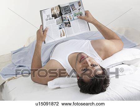 Stock Image - Man holding a magazine while lying in bed. Fotosearch