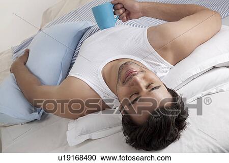 Man lying in bed with a cup of coffee View Large Photo Image Stock Image - Man lying in bed with a cup of coffee. Fotosearch