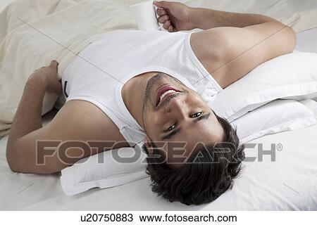 Stock Image - Man lying in bed with a cup of coffee. Fotosearch