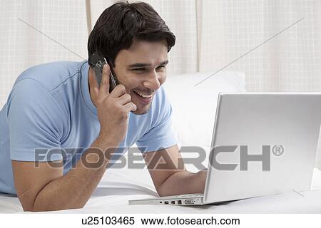 Man talking on the phone while working on a laptop View Large Photo Image Stock Photography - Man talking on the phone while working on a laptop. Fotosearch