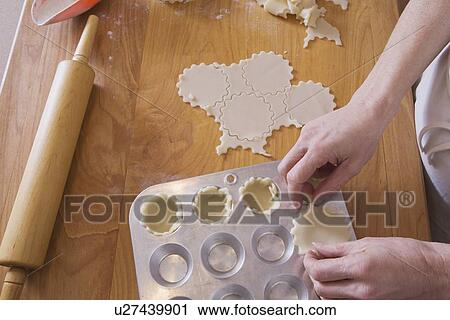 Stock Image - person placing dough into muffin pan on cutting board with rolling pin. Fotosearch