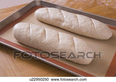 Stock Image - two uncooked loaves of bread on a baking sheet. Fotosearch