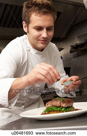 Stock Image - Chef Adding Seasoning To Dish In Restaurant Kitchen. Fotosearch