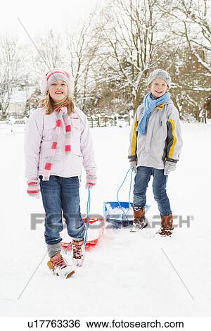 Stock Photograph - Children Pulling Sledge Through Snowy Landscape. Fotosearch