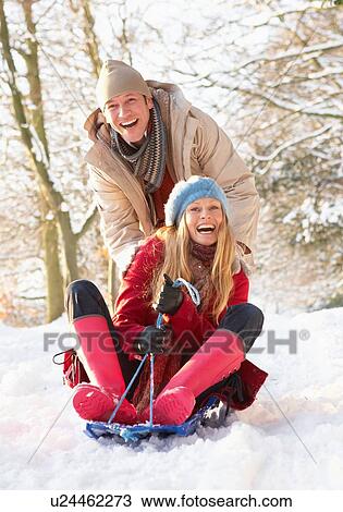 Stock Image - Couple Sledging Through Snowy Woodland. Fotosearch