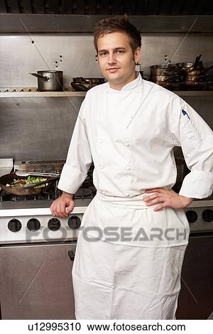 Stock Image - Male Chef Standing Next To Cooker In Restaurant Kitchen. Fotosearch