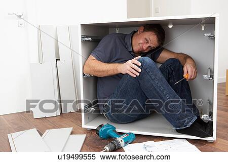 Stock Photography - Man Trapped Whilst Assembling Flat Pack Furniture. Fotosearch