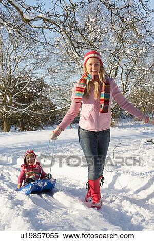 Stock Photography - Mother Pulling Daughter On Sledge Through Snowy Landscape. Fotosearch