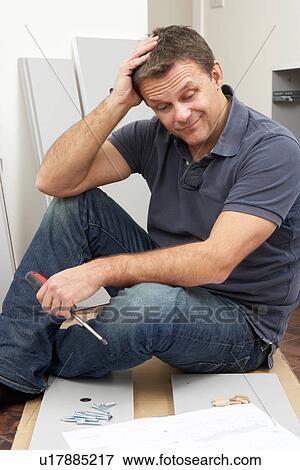 Stock Photo - Puzzled Man Assembling Flat Pack Furniture. Fotosearch