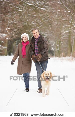 Stock Photo - Senior Couple Walking Dog Through Snowy Woodland. Fotosearch