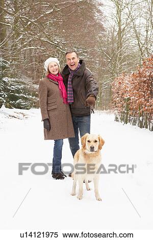 Stock Photography - Senior Couple Walking Dog Through Snowy Woodland. Fotosearch
