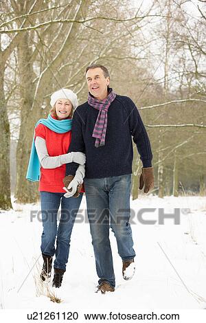 Stock Image - Senior Couple Walking Through Snowy Woodland. Fotosearch
