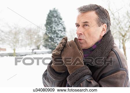 Stock Photo - Senior Man Standing Outside In Snowy Landscape Warming Hands. Fotosearch