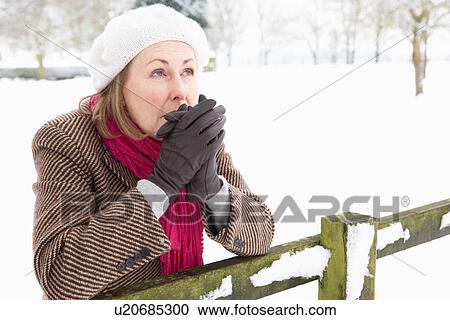 Stock Image - Senior Woman Standing Outside In Snowy Landscape Warming Hands. Fotosearch