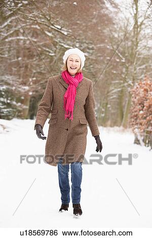 Stock Photograph - Senior Woman Walking Through Snowy Woodland. Fotosearch