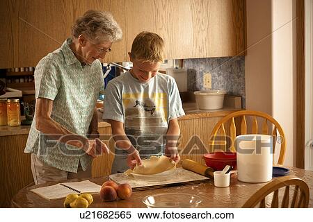 Stock Photography - 12 year old boy placing pastry into pie plate with great grandmother; Redvers, Saskatchewan, Canada. Fotosearch