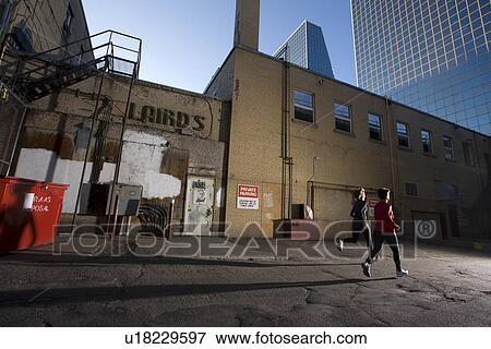Stock Photo - 2 women running at rear of downtown buildings, Regina, Saskatchewan. Fotosearch