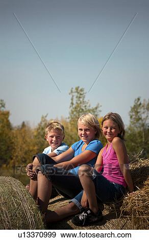 Stock Photo - 3 farm kids seated on bales; Redvers, Saskatchewan, Canada. Fotosearch