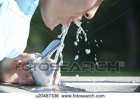 Stock Photograph - Asian woman drinks from water fountain in Assiniboine Park, Winnipeg, Canada. Fotosearch