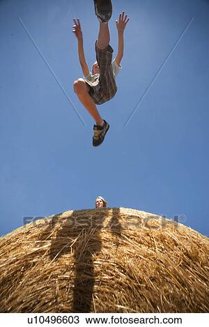Stock Image - Boy (12) mid jump on straw bales; Redvers, Saskatchewan, Canada. Fotosearch