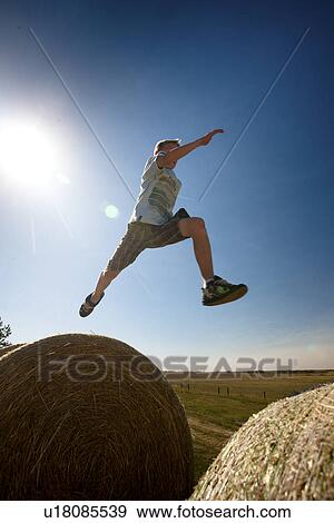 Stock Photo - Boy (12) mid jump on straw bales; Redvers, Saskatchewan, Canada. Fotosearch