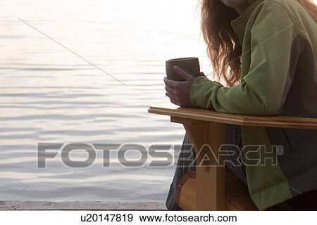 Stock Photo - Close up of arm and coffee cup on deck chair beside Clear Lake, Manitoba. Fotosearch