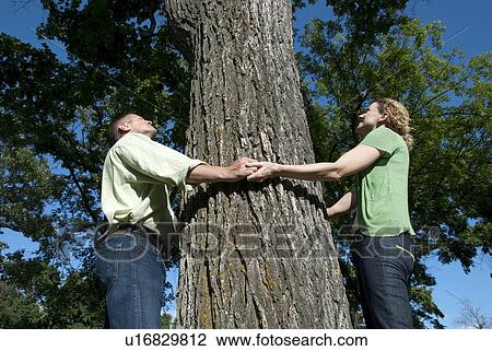 Stock Image - Couple hold hands around large trees, Assiniboine Park, Winnipeg, Canada. Fotosearch
