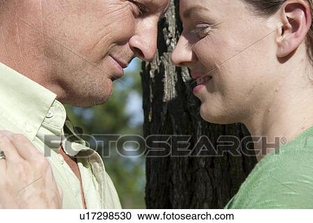 Stock Image - Couple in 40's with heads together besdie tree in Assiniboine Park, Winnipeg, Canada. Fotosearch