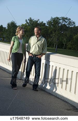 Stock Photo - Couple in their 40's strolling over pedstrian bridge in Assiniboine Park, Winnipeg, Canada. Fotosearch