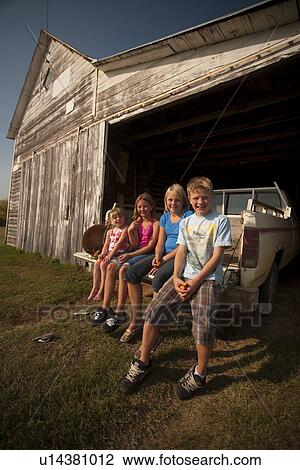 Stock Image - Cousins (five, ten, twelve and twelve) seated on the tailgate of pick-up truck; Redvers, Saskatchewan, Canada. Fotosearch