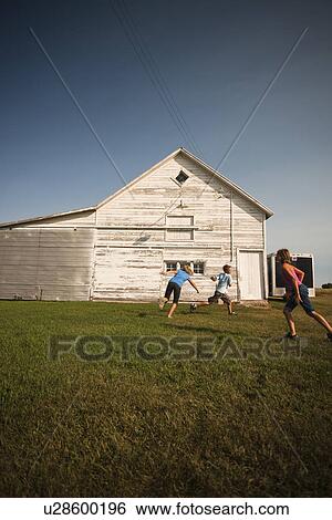 Stock Photograph - Cousins (ten, twelve and twelve) play tag in farmyard; Redvers, Saskatchewan, Canada. Fotosearch