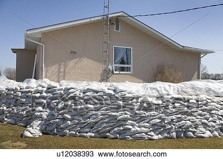Stock Image - Dyke of sandbags around rural home to protect from Red River floodwaters, rural Manitoba. Fotosearch