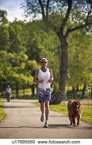 Stock Image - Female runner in park with dog, Regina, Saskatchewan. Fotosearch