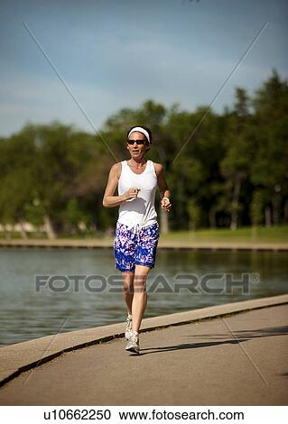 Stock Image - Female runner lakeside in park, Regina, Saskatchewan. Fotosearch