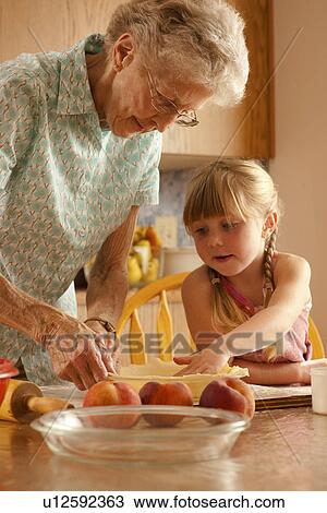 Stock Image - Five year old girl helping great grandmother prepare pastry; Redvers, Saskatchewan, Canada. Fotosearch