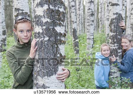 Stock Photograph - Girl foreground beside tree, girl and woman background beside tree, Manitoba, Canada. Fotosearch