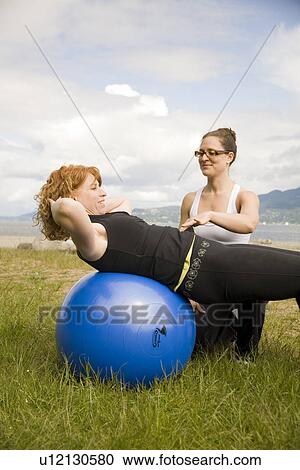 Stock Image - Instructor and woman using exercise ball on beach, Vancouver, BC. Fotosearch