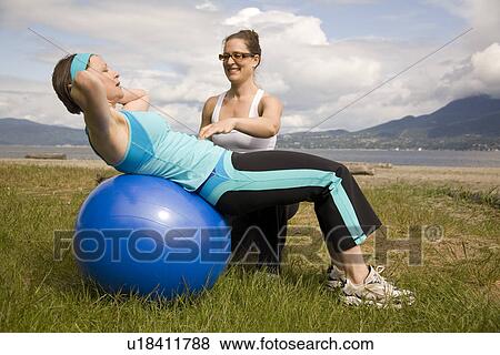 Stock Photo - Instructor and woman using exercise ball on beach, Vancouver, BC. Fotosearch