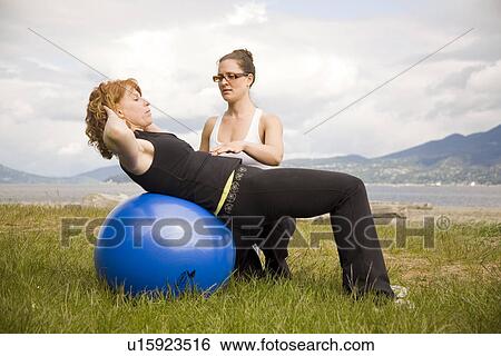 Stock Photograph - Instructor and woman using exercise ball on beach, Vancouver, BC. Fotosearch