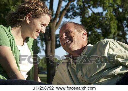 Stock Image - Laughing couple seated on grass in Assiniboine Park, Winnipeg, Canada. Fotosearch