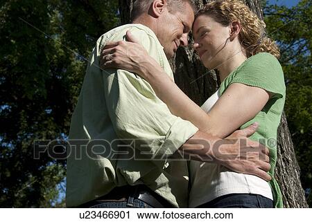 Stock Image - Low angle, couple embracing beside tree in park, Winnipeg, Canada. Fotosearch