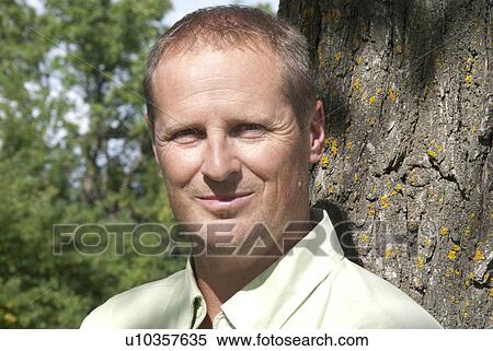 Stock Photography - Man in 40's standing beside tree, Winnipeg, Canada. Fotosearch