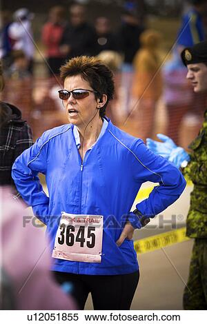 Stock Photography - Middle aged woman in blue jacket catching her breath after marathon, Regina, Saskatchewan. Fotosearch