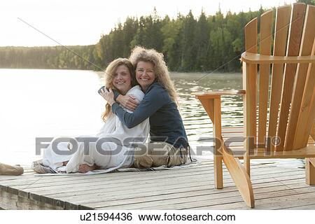 Stock Photograph - Mom and adult daughter seated on dock at Clear Lake, Manitoba, Canada. Fotosearch