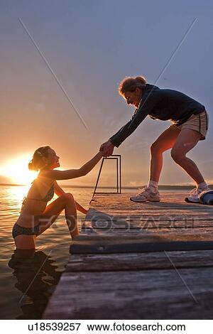 Stock Photo - Mom helps tween girl up out of lake, sunset, Riding Mountain National Park, Manitoba, Canada. Fotosearch