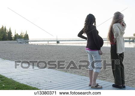 Stock Image - Pregnant woman and friend on beach boardwalk, Clear Lake, Manitoba, Canada. Fotosearch
