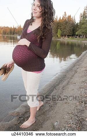 Stock Photograph - Pregnant woman holding sandals at shore of Clear Lake, Manitoba, Canada. Fotosearch