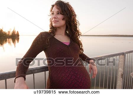 Stock Photography - Pregnant woman leans on railing, sunset, Clear Lake, Manitoba, Canada. Fotosearch