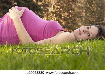 Stock Image - Pregnant woman lying back on grass, Manitoba, Canada. Fotosearch